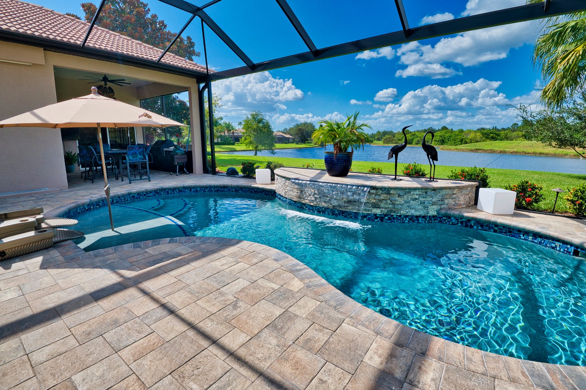 A pristine screened-in backyard pool with travertine deck and lake view